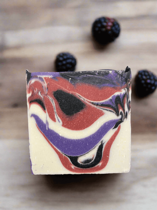 Vegan Black Raspberry Vanilla soap with marbled design, surrounded by fresh blackberries on a wooden surface.