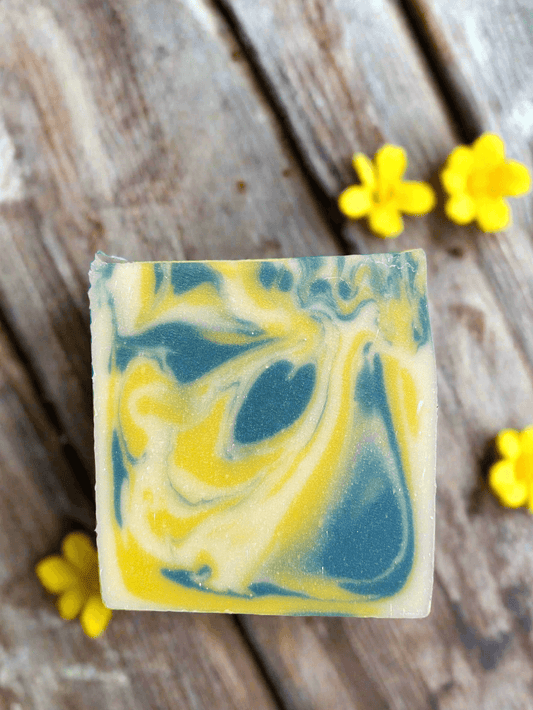 Organic honeysuckle soap with colorful swirls, surrounded by yellow flowers on a wooden surface.