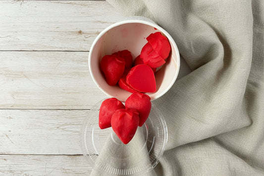 Strawberry Wax Melts shaped like hearts in a white cup on a wooden surface.