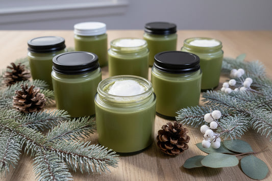Fir and Frost Beard Butter jars surrounded by pinecones and winter greenery on a wooden table.