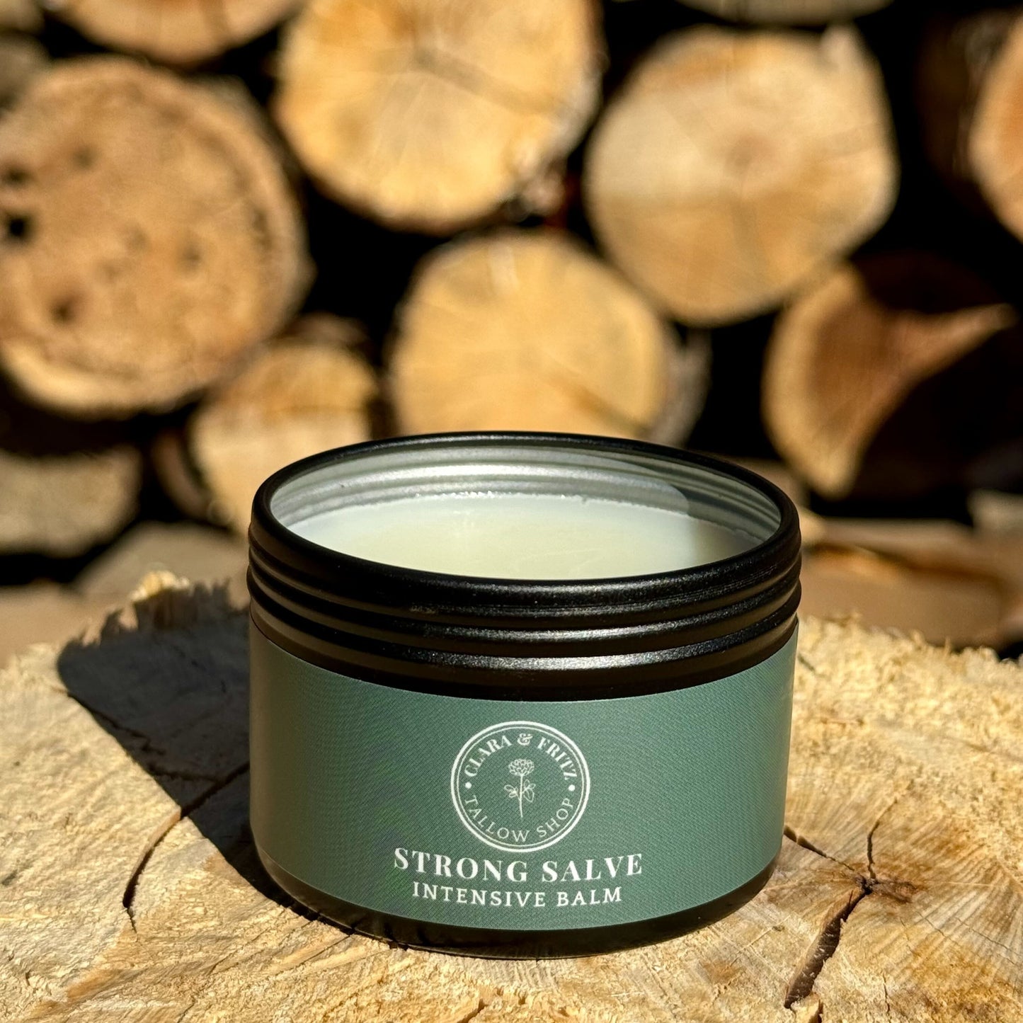 Strong Salve tallow-based balm displayed on a wooden surface with logs in the background.