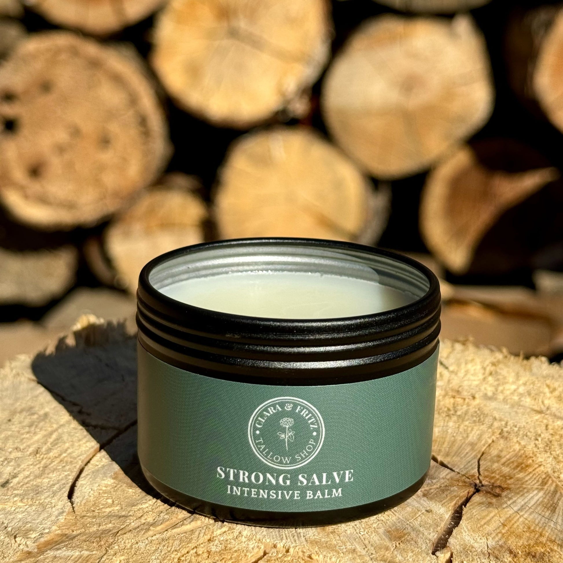Strong Salve tallow-based balm displayed on a wooden surface with logs in the background.